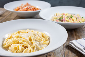 A view of three pasta dishes on a table, featuring fettuccine Alfredo.