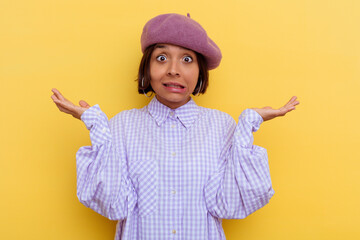Young mixed race woman wearing a beret isolated on yellow background doubting and shrugging...