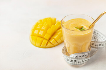 Smoothie or milkshake with a mango in a glass on the table. Measuring tape. Diet nutrition