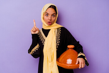 Young Moroccan woman holding a tajine isolated on purple background having some great idea, concept of creativity.