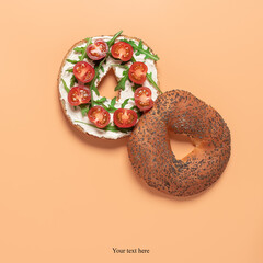 Fresh bagel sandwich with cream cheese, cherry tomato and arugula. Pastel peach background. Top...