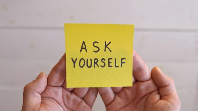 ASK YOURSELF written on a yellow sticker. Man hands holding a yellow sticky note paper on a white background