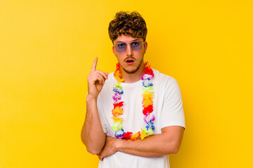 Young caucasian man wearing a Hawaiian party stuff isolated on yellow background having some great...