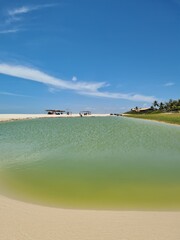 Lagoa de águas esverdeadas rodeada e areia branca em dia de céu azul
