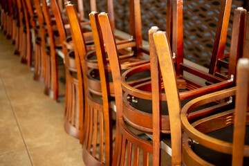 Fototapeta na wymiar A view inside a closed restaurant dining room, featuring a line of chairs turned over on the tables. 