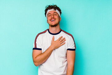 Young sport caucasian man isolated on blue background laughs out loudly keeping hand on chest.