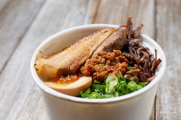 A closeup view of ingredients in a tonkatsu ramen to-go cup container.