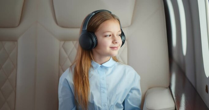 Preteen girl in headphones sitting in airplane looking through window