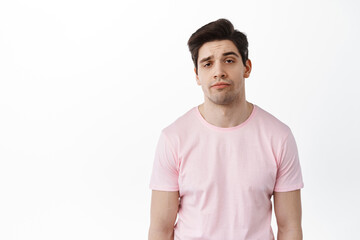 Indifferent and careless adult man staring at camera with unamused bored expression, standing displeased and uninterested against white background