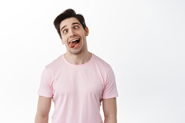 Funny man showing grimaces and tongue, making fun faces playfully, fool around, standing against white background