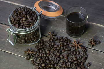 Creative vintage background.Coffee beans in jar with black coffee in glass on rustic wooden table.