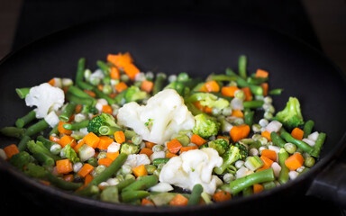 stewed vegetables (carrots, beans, peas, broccoli, cabbage, onions) lie in a black pan close-up