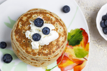 Stack of pancakes with butter cream and blueberries on a plate with a pattern