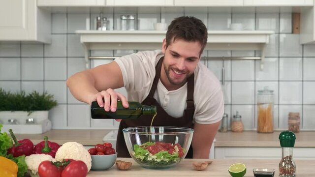 Vegan Cooking, Male Chef, Healthy Eating, Food Delivery. Male chef adding olive oil to vegan salad while standing in kitchen at home