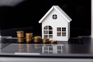 Small house on a laptop and coins close-up. Mortgage concept