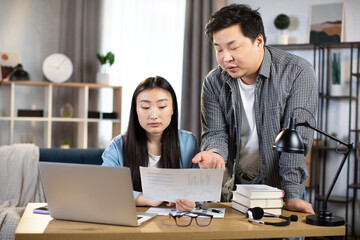 Asian man and woman analyzing and discussing graphs and charts at office. Young colleagues using modern gadgets for work. Cooperation concept.