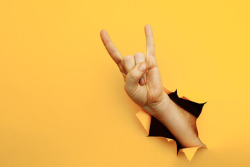 Male hand making a rock and roll gesture, party, goat on a yellow background