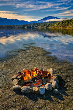 An open fire on a lake shore with blue sky and clouds in the distance