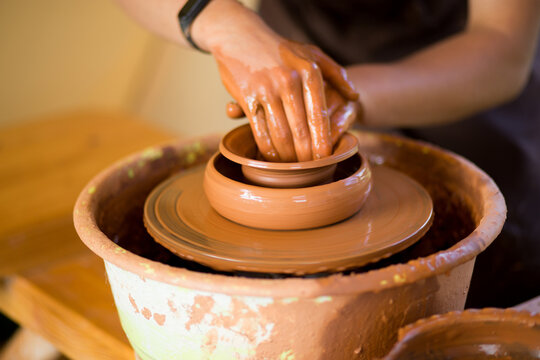 Hands of potte makes pottery dishes on potter's wheel. Sculptor in workshop makes clay product closeup