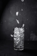 Crushed cocktail ice falling into a collins highball glass, dark backdrop
