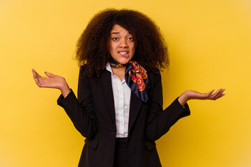 Young African American air hostess isolated on yellow background confused and doubtful shrugging...