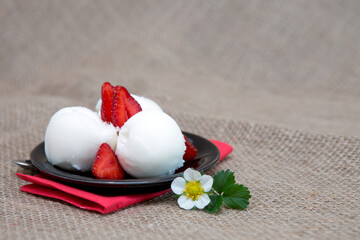 Ice cream with strawberry on black plate.