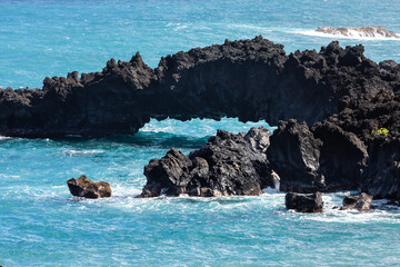 Turquoise water and brilliant foam swirl around in arch in the volcanic rock at Waianapanapa State Park on the north shore of Maui near Hana, Hawaii
