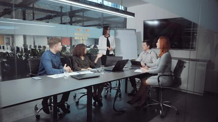 Woman standing by flipchart and reporting during business meeting in office. Multiethnic team discussing project and planning strategy. Concept of analysis