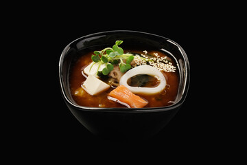 Miso soup with salmon and squid, broth, wakame seaweed, shiitake mushrooms, tofu cheese, green onions, leeks, sesame seeds. Japanese food. Isolated on black background