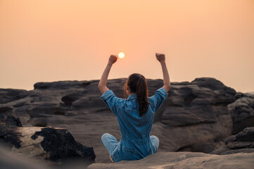 Happy woman in jean shirt raising arms and watching the sunset on rock canyon