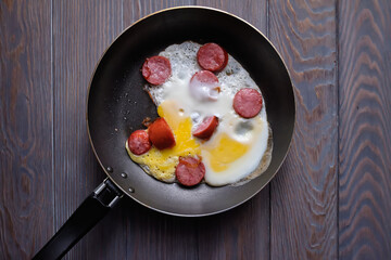 fried egg with sausage in a frying pan on a wooden table