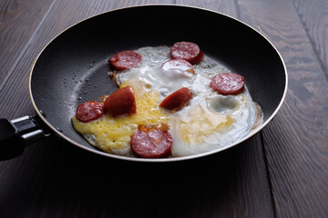 fried egg with sausage in a frying pan on a wooden table