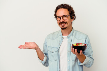 Young caucasian man eating a ramen isolated on white background showing a copy space on a palm and...