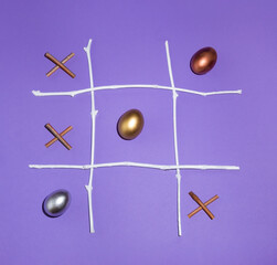 2021 Easter eggs are a winning combination. X O game made of golden, silver and bronze eggs and natural twigs on purple background. Creative tic tac toe game idea. 