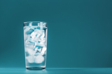 Ice cubes in a glass with crystal clear water on a blue background.