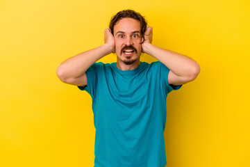 Fototapeta na wymiar Young caucasian man isolated on yellow background covering ears with hands trying not to hear too loud sound.