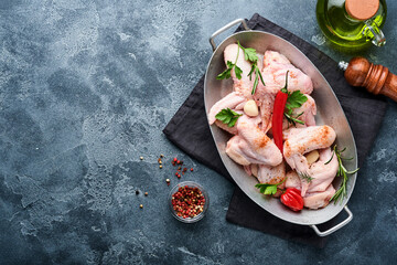 Raw chicken wings in metal pan or bowl with spices and ingredients for cooking on dark grey slate, stone or concrete background. Raw meat with spices at black table. Top view. Mock up.