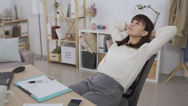 asian woman ceo sitting back and relaxing on swivel chair, staring at office ceiling while thinking about her work plan.