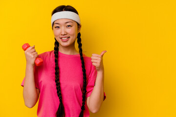Young sport chinese woman isolated on yellow background smiling and raising thumb up