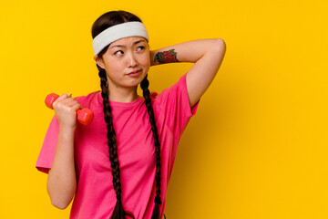 Fototapeta na wymiar Young sport chinese woman isolated on yellow background touching back of head, thinking and making a choice.