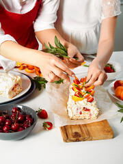 Meringue roll with a delicate air cream, mint and fruit filling of strawberries and peaches. Pavlova summer sweet dessert. Summer baking. Copy space. Mom and daughter prepare meringue roll.