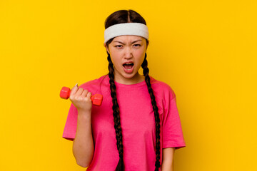 Young sport chinese woman isolated on yellow background screaming very angry and aggressive.