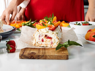 Meringue roll with a delicate air cream, mint and fruit filling of strawberries, peaches and mint. Pavlova summer sweet dessert. Berry dessert on the background of a woman. Summer baking. Copy space.