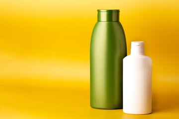 Plastic green and white cosmetic bottles without label on yellow background.