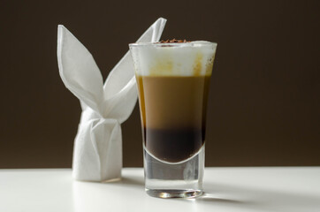 Coffee drink shot with a nutty note with fluffy milk foam, decorated with chocolate shavings, served with an Easter bunny-shaped napkin