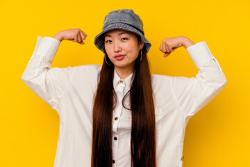 Young chinese woman isolated on yellow background showing strength gesture with arms, symbol of feminine power
