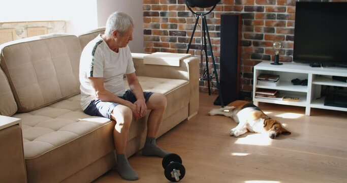 adult man and mature senior working his body with dumbbell - one man hapy training indoors sitted on the sofa. High quality 4k footage