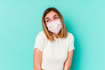 Young woman wearing a mask for virus isolated on blue background dreaming of achieving goals and...