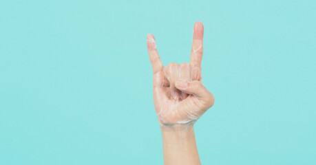 Hand is devil horns or rock hand sign and have foam soap bubbles on a green mint or Tiffany Blue background.isolated