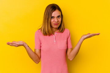 Young caucasian skinny woman isolated on yellow background doubting and shrugging shoulders in questioning gesture.